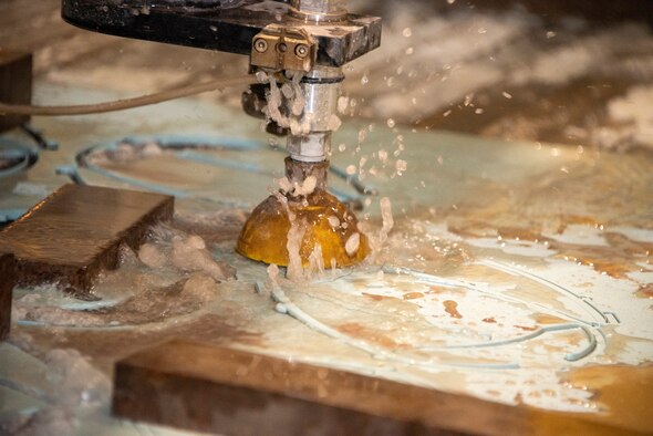 A water jet cuts through old aircraft material to create parts for face shields March 31, 2020, at Travis Air Force Base, California. 60th Air Mobility Wing Phoenix Spark, 60th Maintenance Squadron and 60th Bioenvironmental Engineer Squadron collaborated to come up with easy-to-manufacture personal protective equipment for David Grant USAF Medical Center personnel. (U.S. Air Force photo by Tech. Sgt. Traci Keller)