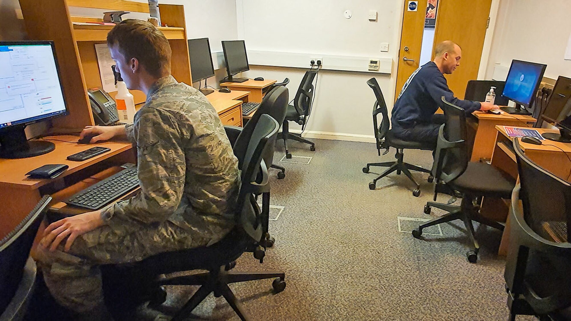 Airman Gabriel Townsend and Matthew Hartwell, both 100th Civil Engineer Squadron firefighters, practice physical distancing as they complete online trainiing April 7, 2020, at RAF Mildenhall, England. During the COVID-19 lockdown, the firefighters are taking extra precautions both in and out of the fire station to ensure the health and safety of both themselves and the base community. (Courtesy photo by Matthew Thorpe)