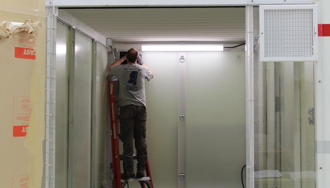 Employees from the U.S. Army Engineer Research and Development Center’s Directorate of Public Works hang a door on a makeshift hospital room, or Containerized Medical Solution, constructed of wood and a metal frame, March 31, 2020. The team has been tasked with building out designs developed by the USACE Hunstville District and assessing their feasibility. The team is working to examine converting a portable storage unit into a one-bed hospital room versus constructing a wooden and metal room from scratch for the emergency response to the COVID-19 outbreak.