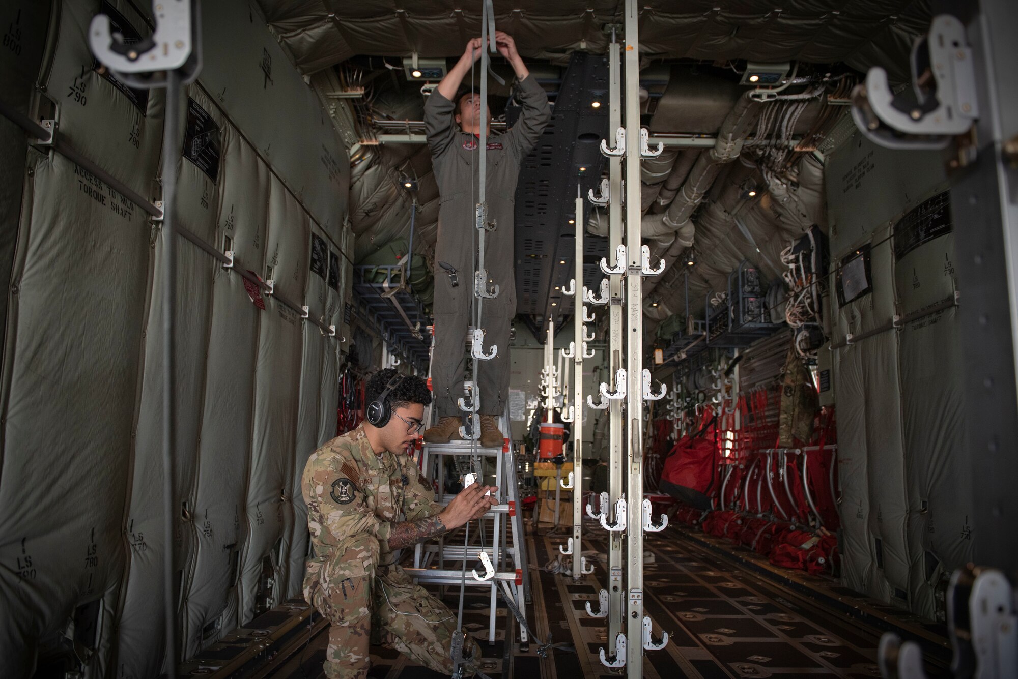 (From top to bottom) Senior Airman Jaime Suarez and Senior Airman Antonio Parks, both 36th Airlift Squadron C‐130J Super Hercules loadmasters, hang a litter strap in a C‐130J to execute an aeromedical evacuation scenario during the Yokota C‐130J Tactics Rodeo April 3, 2020, at Yokota Air Base, Japan.
