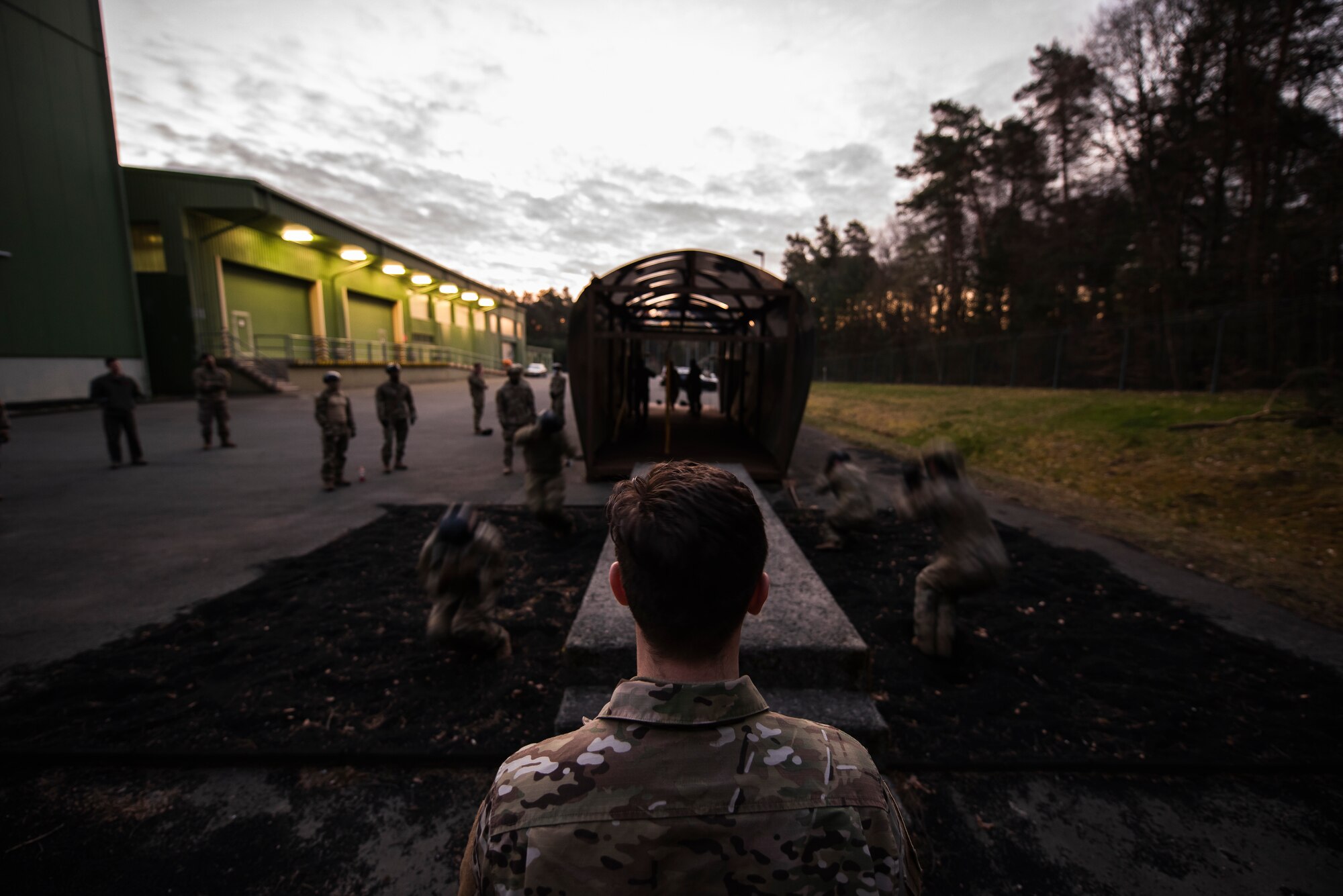 Four Airmen are jumping off of an elevated platform and rolling on the ground; they are blurry because of the motion.