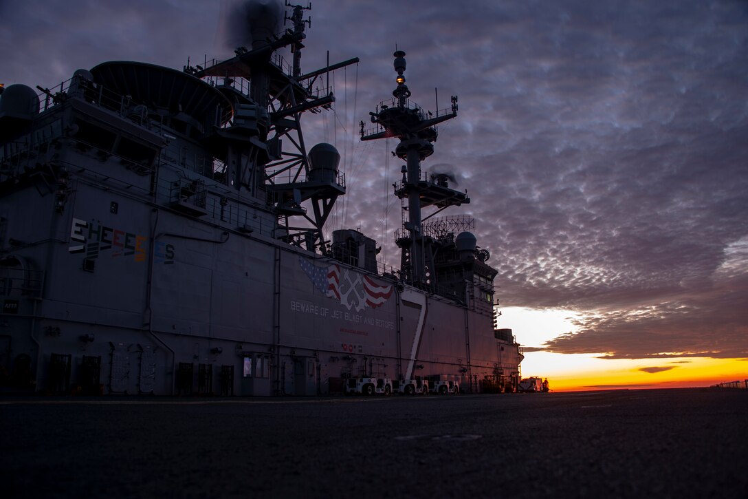 A military ship sails at twilight.