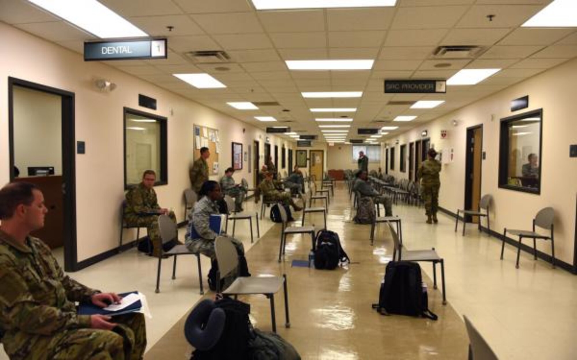 Photo of service members waiting in chairs, six-feet a part, to in-process.