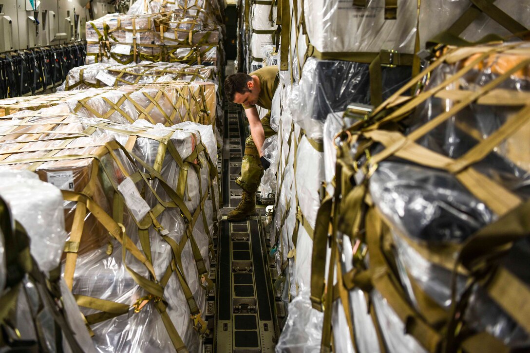 An airman bends down in between a large group of pallets.