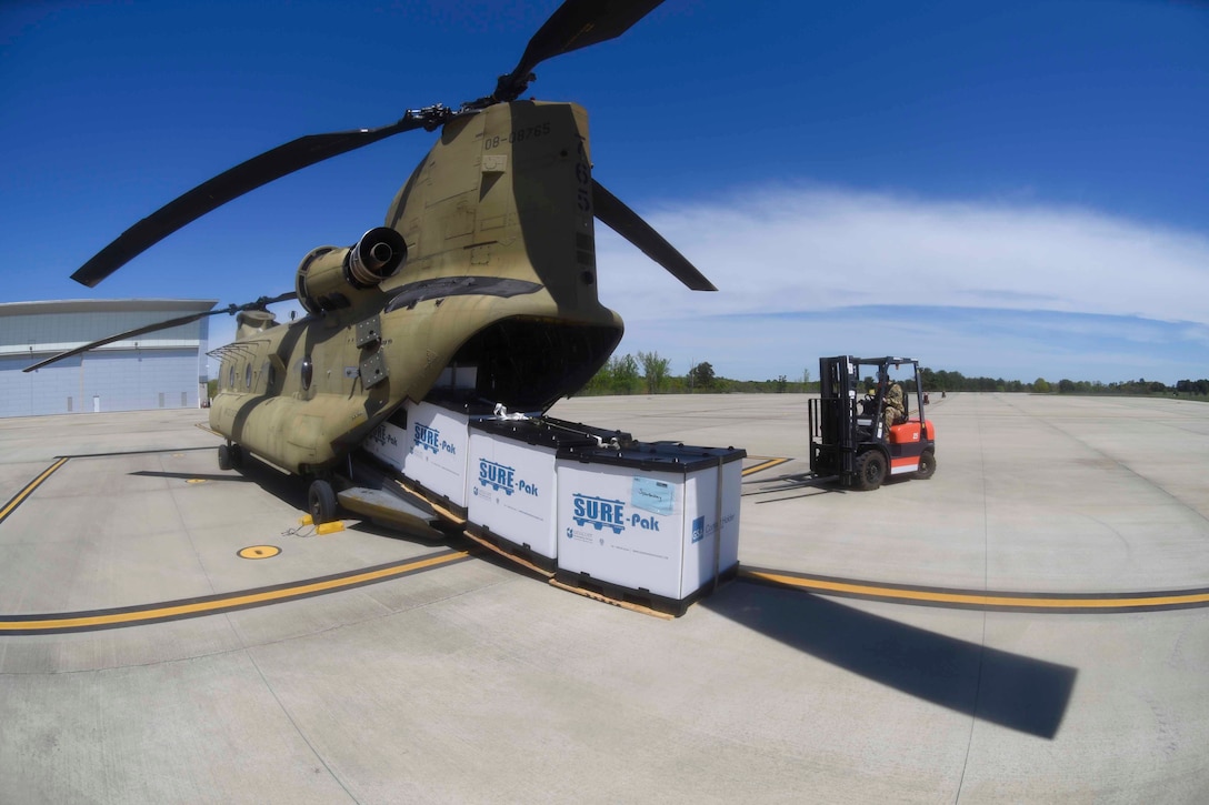 A soldier uses a forklift to unload large parcels from the back of a helicopter.