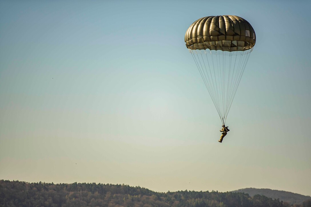 An airman descends in the sky with his parachute open.