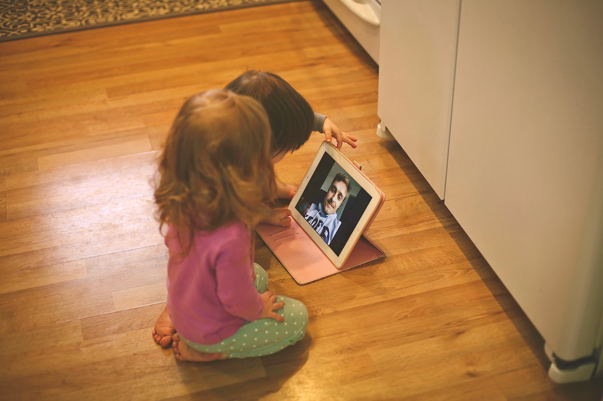 Two young children use an IPad to FaceTime with their father.