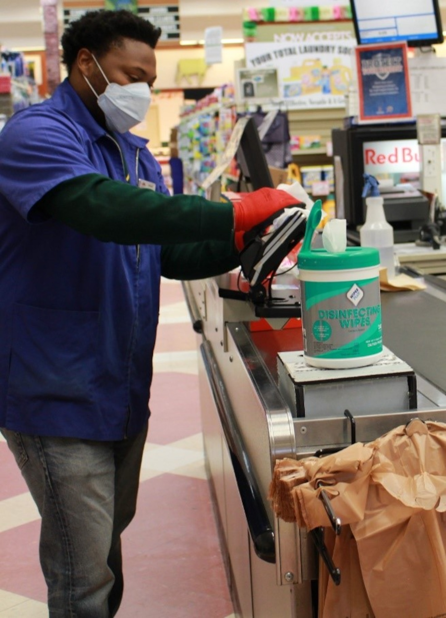 A commissary store worker wears personal protective equipment as he wipes down a checkout area