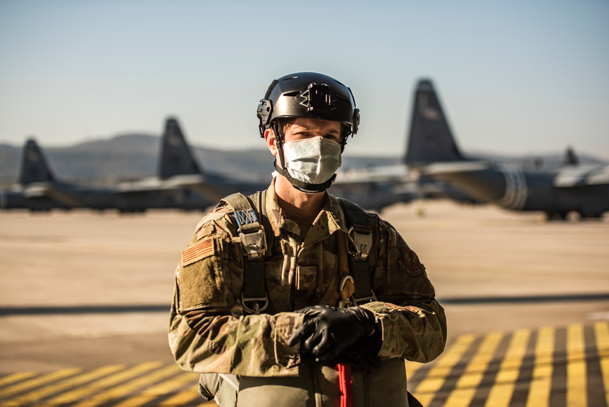 An Airman poses with their parachute on in front of C-130J Super Hercules aircraft.