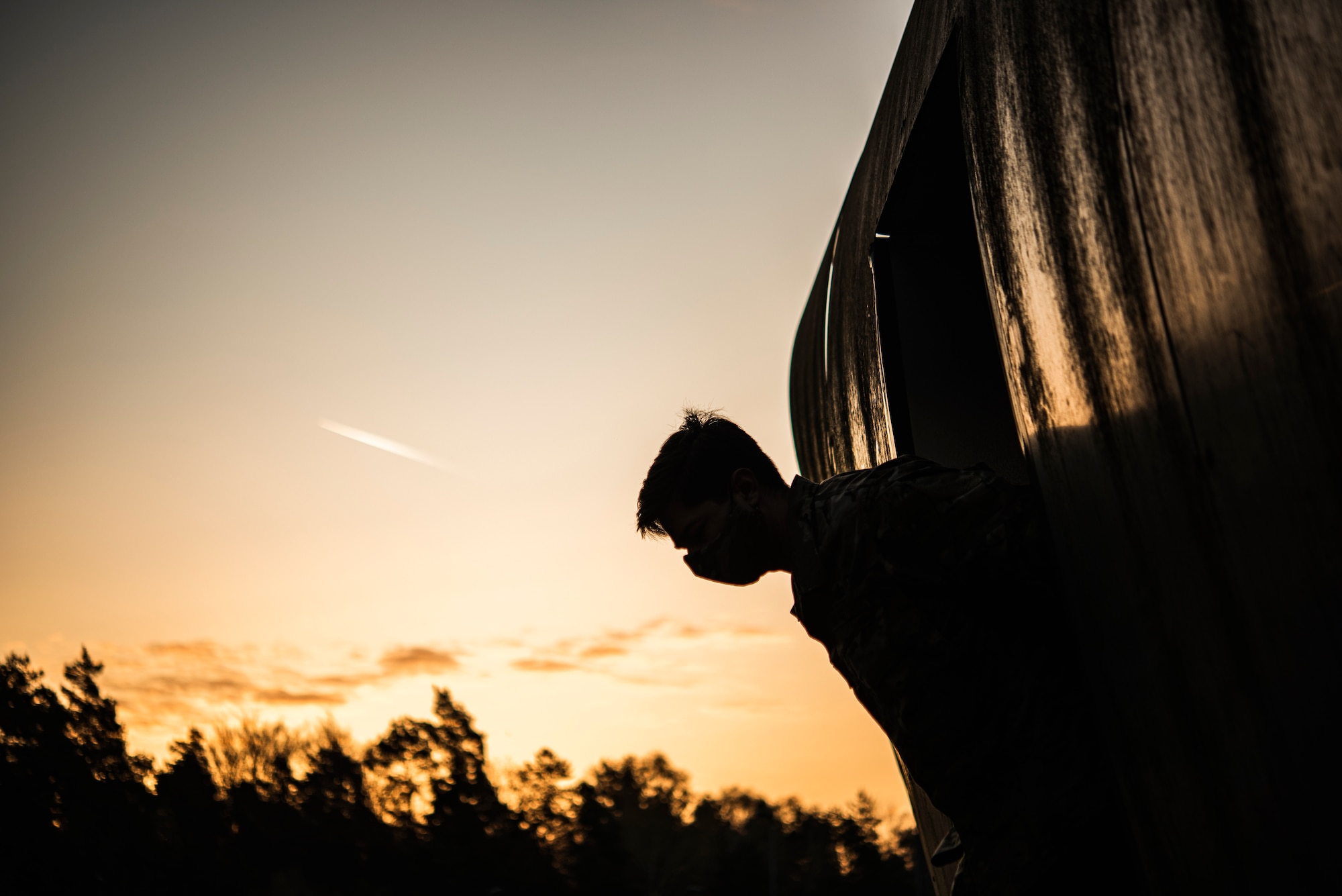 An Airman is silhouetted looking out from a C-130 training model during sunrise.