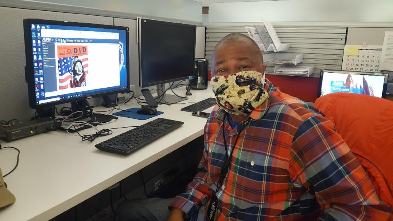 A man wearing a face mask sits in front of a computer monitor.