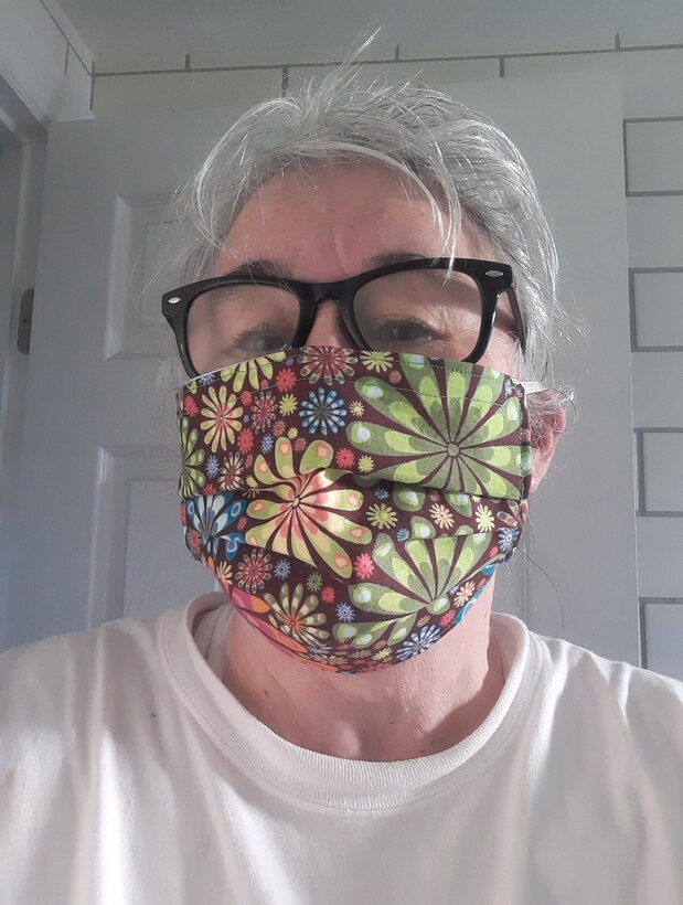A person wearing glasses wears a large face mask with flowers.