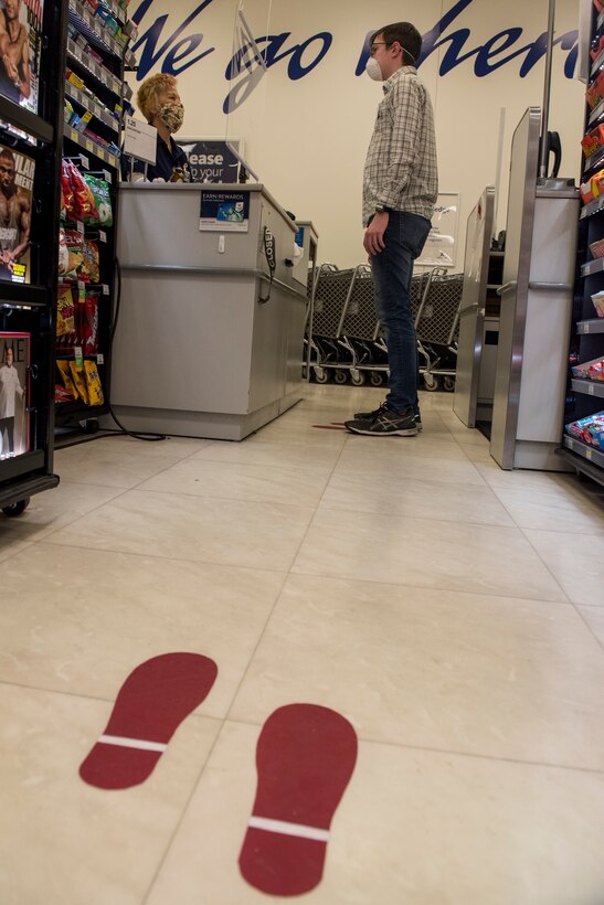 A cashier talks to a customer as they both wear cloth masks