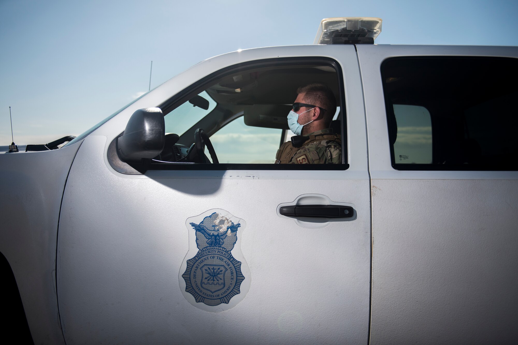 A security forces patrolman sits in his truck while wearing a cloth mask.