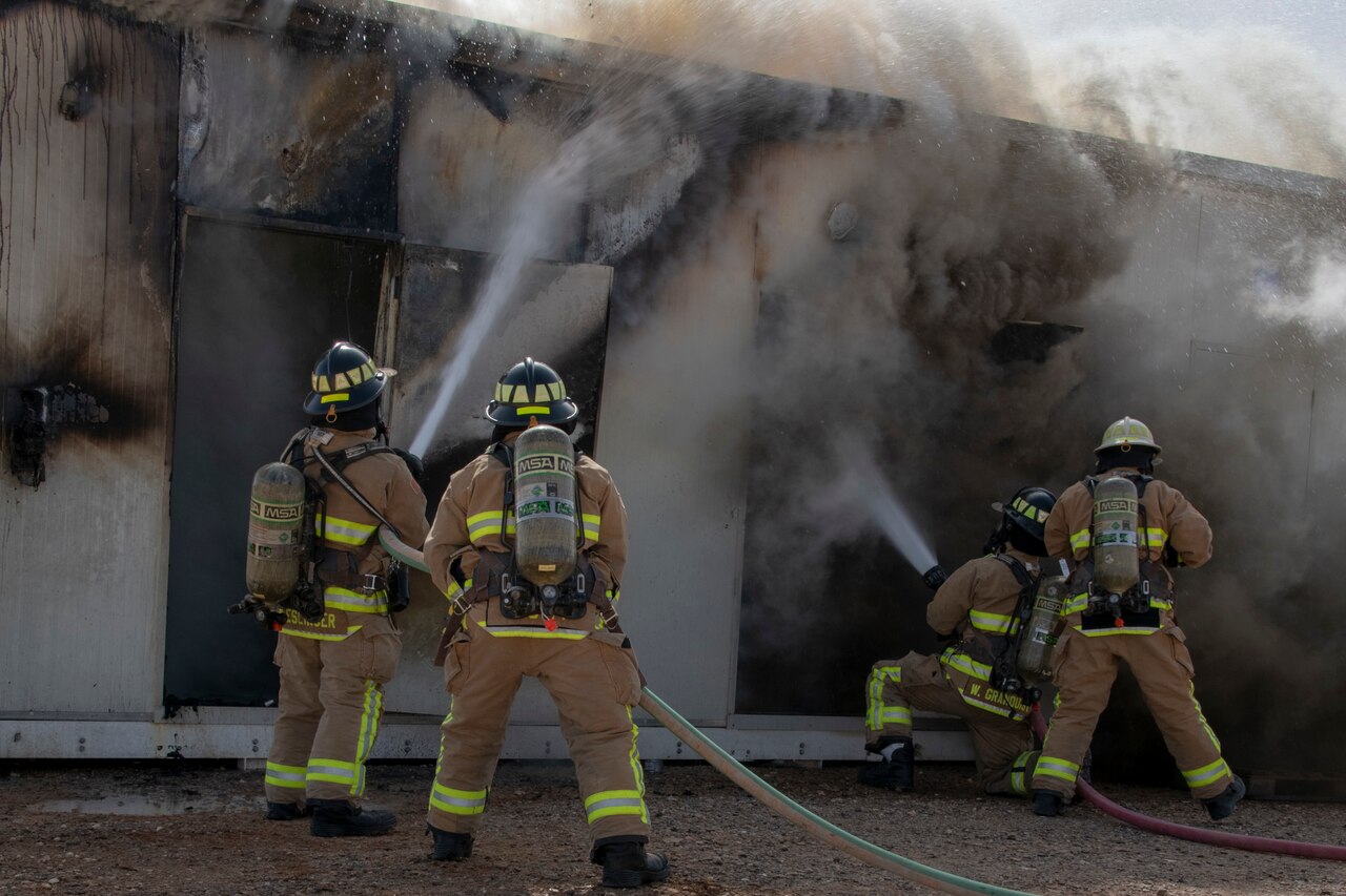 Four firefighters spray a fire with hoses.