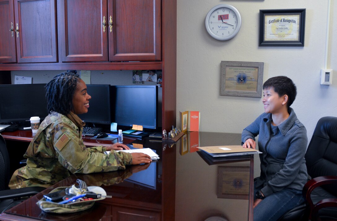 Two women sit across a desk chatting.