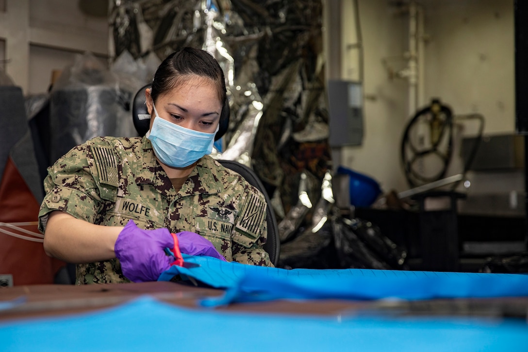 A sailor uses scissors to cut fabric on a table.