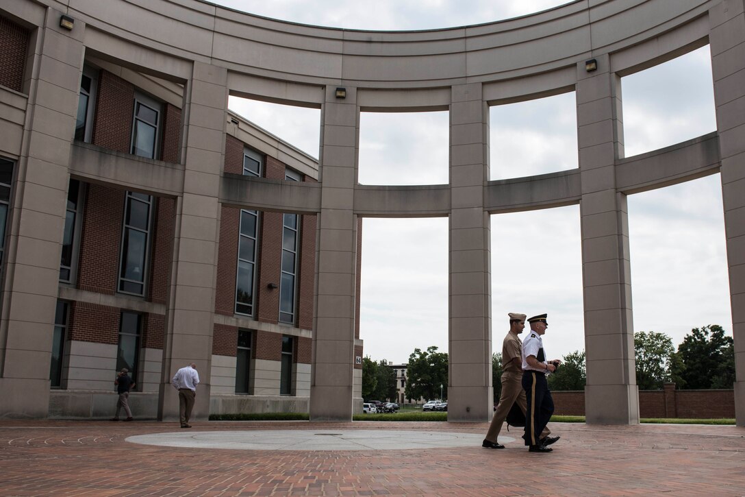 Several individuals in military uniform either stand within or move through a circular colonnade.