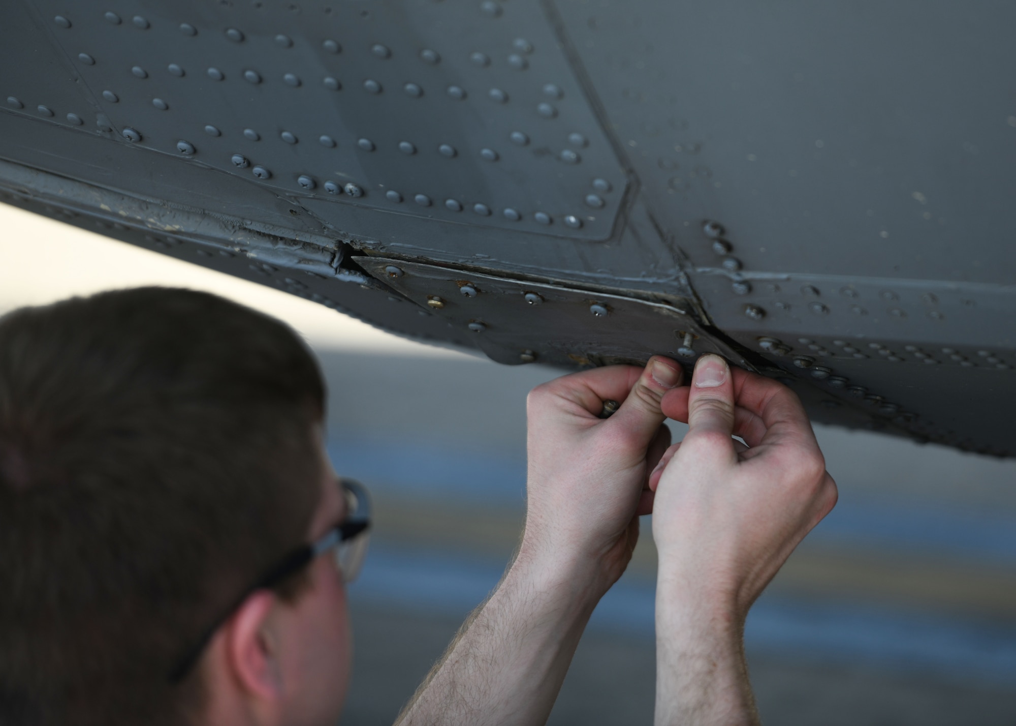 An Airmen pushes on a panel attached to a C-130J Super Hercules.