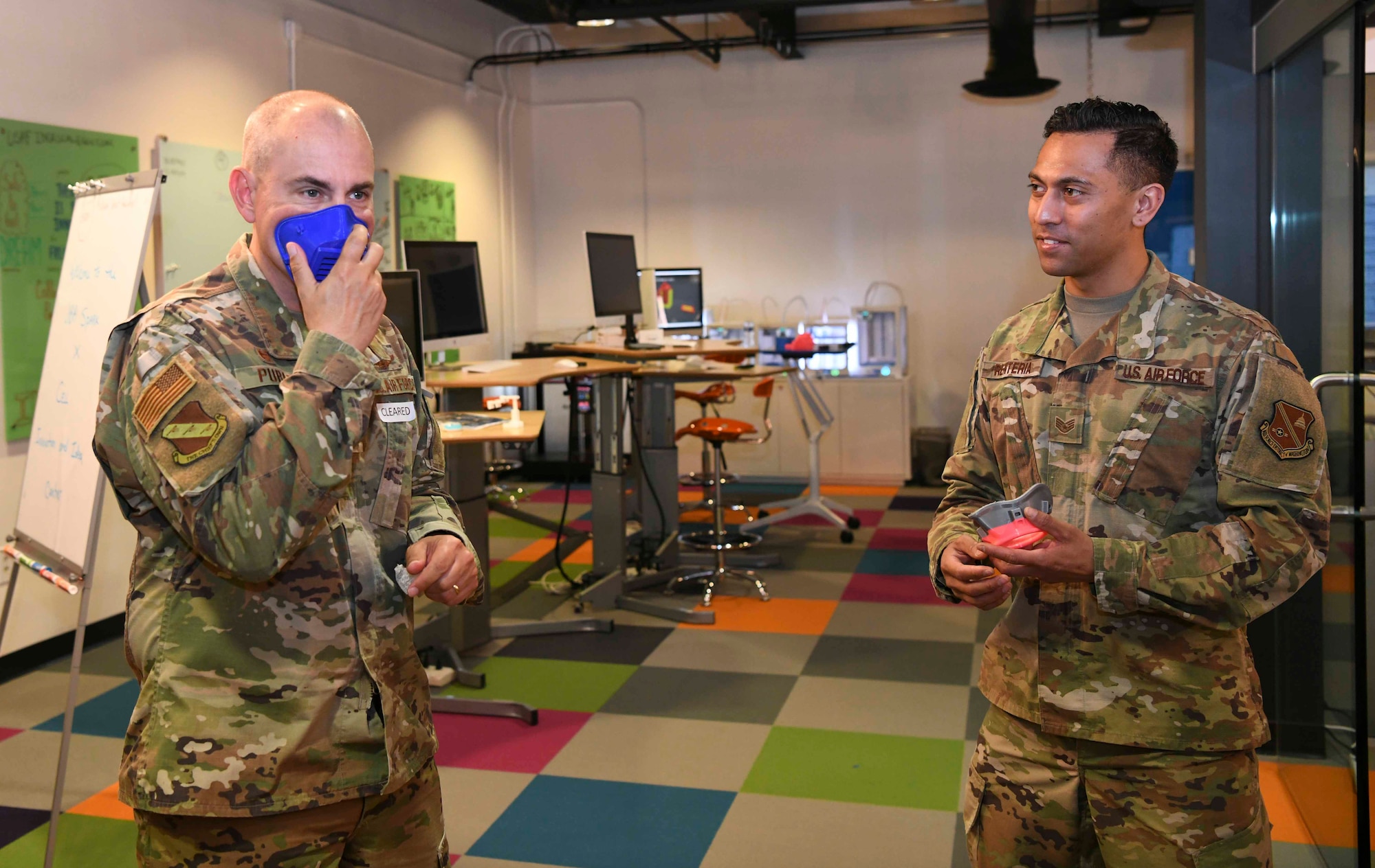 Col. Andrew Purath, 11th Wing and Joint Base Andrews commander, tries on multiple facemasks while Staff Sgt. Andy Keala Anoa’i Renteria, 11th Wing SparkX Cell innovations technician, observes at the SparkX Cell on JBA, Md., Apr. 8, 2020. Each single model of facemask printed takes varying amounts of time to print, with the quickest being three hours and the longest up to eight hours. SparkX Cell team members have been making prototype personal protective equipment in an effort to help prevent the spread of COVID-19.  (U.S. Air Force photo by Airman 1st Class Spencer Slocum)
