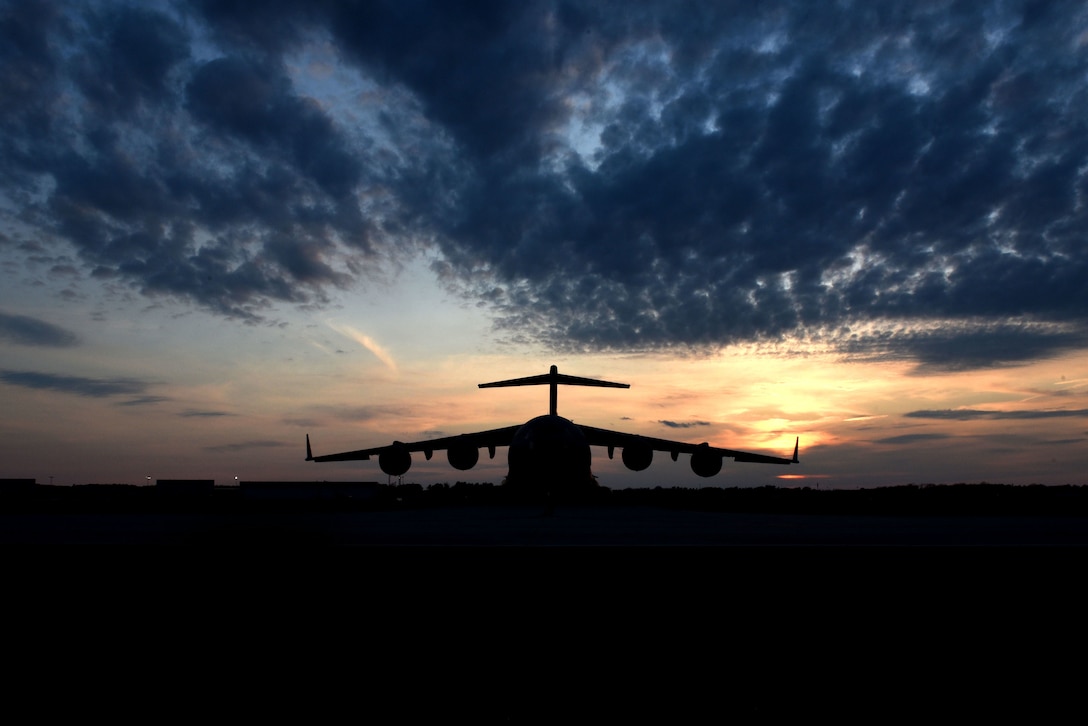 An Air Force aircraft, shown in silhouette, sits on a sunlit flightline.