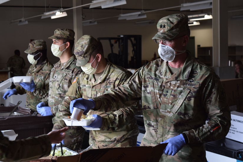 Soldiers wearing medical masks and gloves serve food.