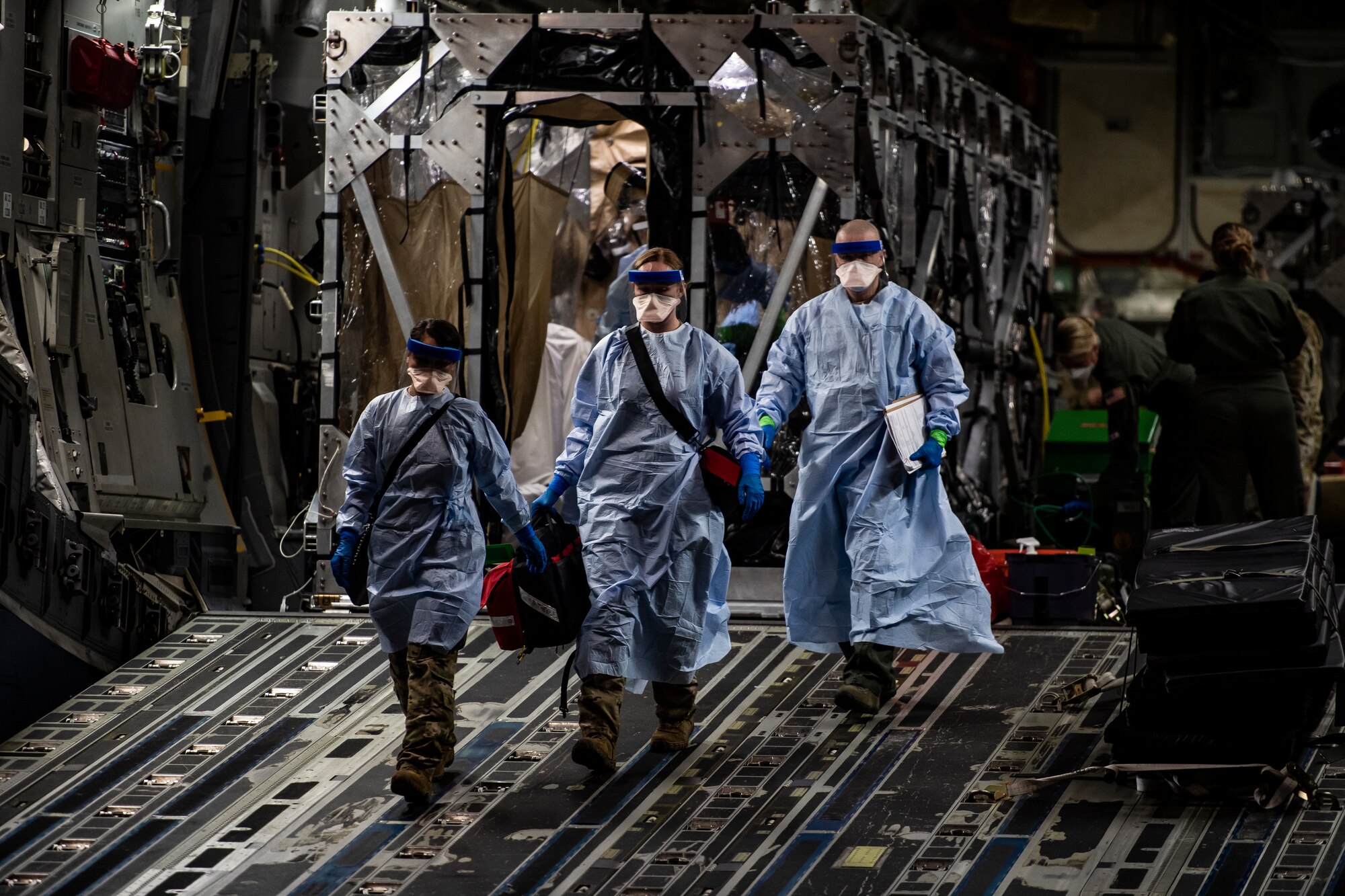 Three U.S. Air Force medical Airmen exit a C-17 Globemaster III aircraft following the first-ever operational use of the Transport Isolation System at Ramstein Air Base, Germany, April 10, 2020. The TIS is an infectious disease containment unit designed to minimize contamination risk to aircrew and medical attendants, while allowing in-flight medical care for patients afflicted by a disease--in this case, COVID-19. (U.S. Air Force photo by Staff Sgt. Devin Nothstine)