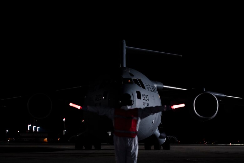 A U.S. Air Force Airman, assigned to the 721st Aerial Port Squadron, marshals a C-17 Globemaster III aircraft transporting three COVID-19 patients from Afghanistan during the first-ever operational use of the Transport Isolation System at Ramstein Air Base, Germany, April 10, 2020. The TIS is an infectious disease containment unit designed to minimize contamination risk to aircrew and medical attendants, while allowing in-flight medical care for patients afflicted by a disease--in this case, COVID-19. (U.S. Air Force photo by Staff Sgt. Devin Nothstine)