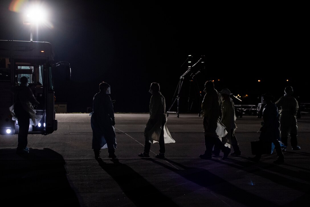 U.S. Air Force Airmen escort COVID-19 patients to a medical bus before transporting them to the Landstuhl Regional Medical Center during the first-ever operational use of the Transport Isolation System at Ramstein Air Base, Germany, April 10, 2020. The TIS is an infectious disease containment unit designed to minimize contamination risk to aircrew and medical attendants, while allowing in-flight medical care for patients afflicted by a disease--in this case, COVID-19. (U.S. Air Force photo by Staff Sgt. Devin Nothstine)