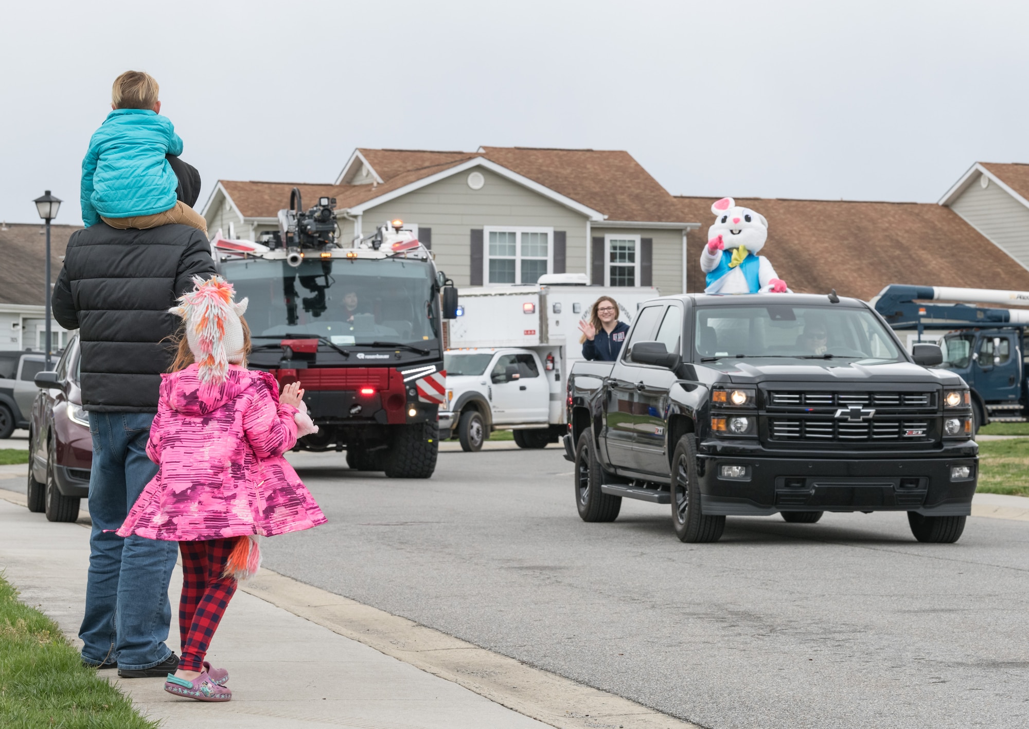 Staff Sgt. David Rhodes, 436th Logistics Readiness Squadron unit deployment manager, along with his son Keegan and daughter Hailey, wait for the Easter Bunny, Tech. Sgt. Jeffrey Seastrand, 436th LRS, to pass their home in Eagle Heights housing April 10, 2020, at Dover Air Force Base, Delaware. A small caravan of USO volunteers, 436th Security Forces Squadron and Civil Engineer Squadron vehicles, escorted the Easter Bunny around the housing area in a vehicle driven by Staff Sgt. Tate Booms, 436th LRS vehicle maintenance, accompanied by his wife Cassidy, USO Delaware volunteer. On this Good Friday, the Easter Bunny and residents observed social distancing to mitigate the spread of COVID-19. (U.S. Air Force photo by Roland Balik)