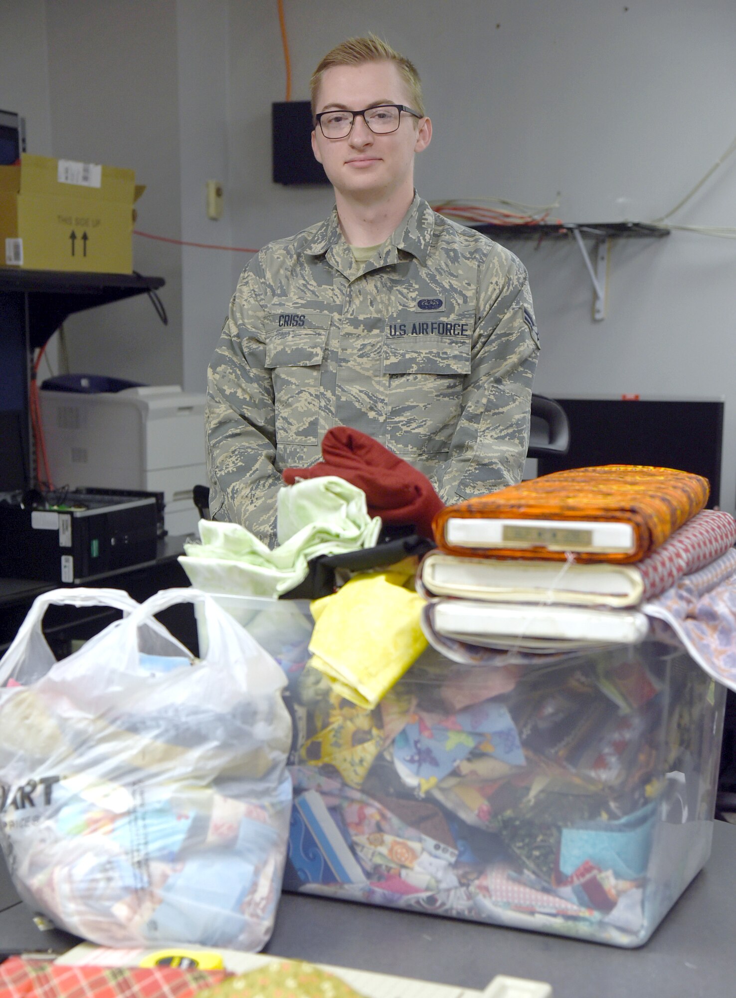 Airman First Class Stephen Criss stands next to a box of donated fabric and materials that he and other volunteers, both military and spouses, are making into face masks. 3-D printed clips for plastic face shields are also being made by volunteers. Several of each product have already been donated to local hospice organizations around the Tinker community, with many more in production to go to other medical facilities. (U.S. Air Force photo/Kelly White)