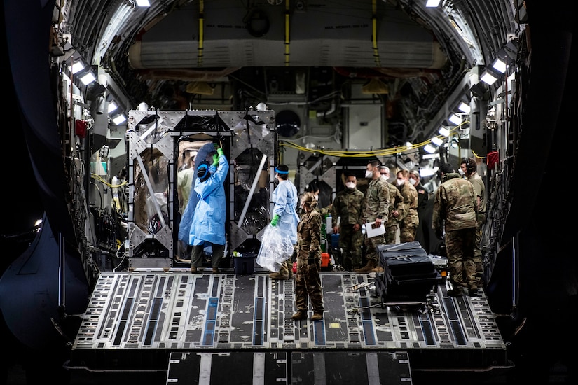 Airmen prepare to remove patients from an isolation chamber in the cargo bay of a large transport jet.