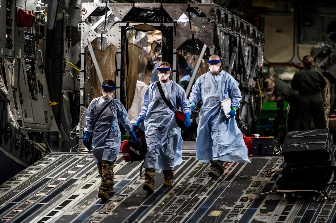 Airmen wearing personal protective gear walk down the open ramp of a large transport jet.