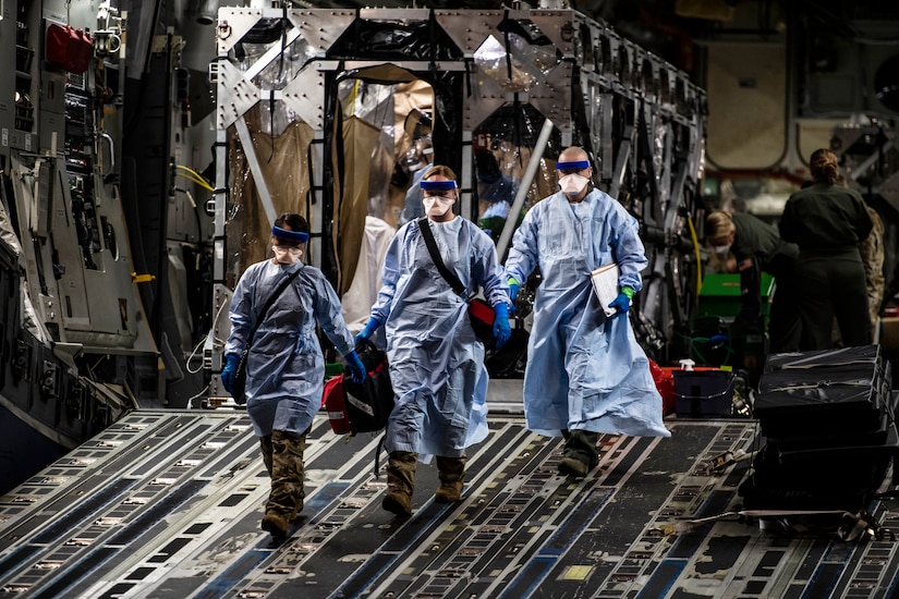 Airmen wearing personal protective gear walk down the open ramp of a large transport jet.