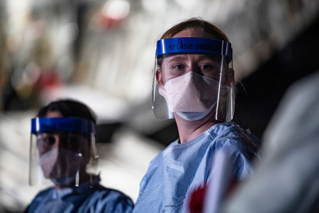 Airmen wearing personal protective gear wait for patient documentation in the cargo bay of a large transport jet.