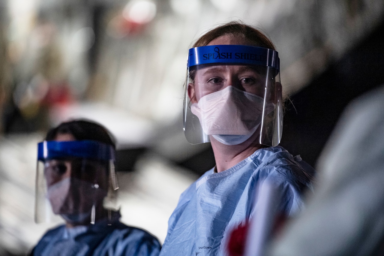 Airmen wearing personal protective gear wait for patient documentation in the cargo bay of a large transport jet.