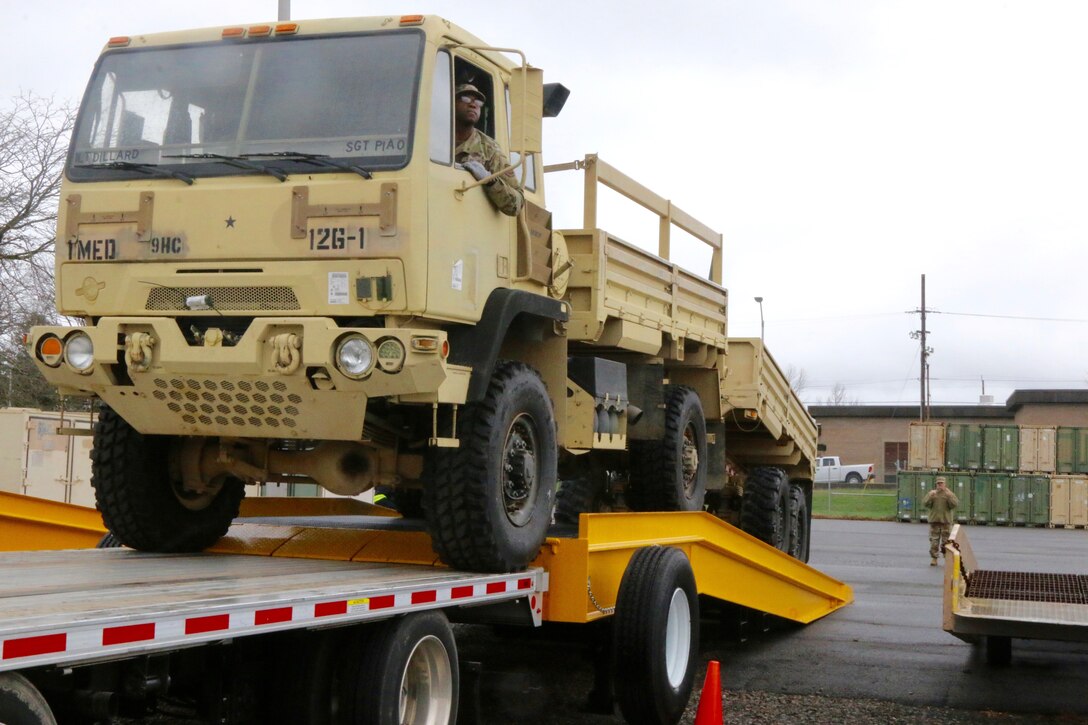 A service member backs a truck down a ramp.