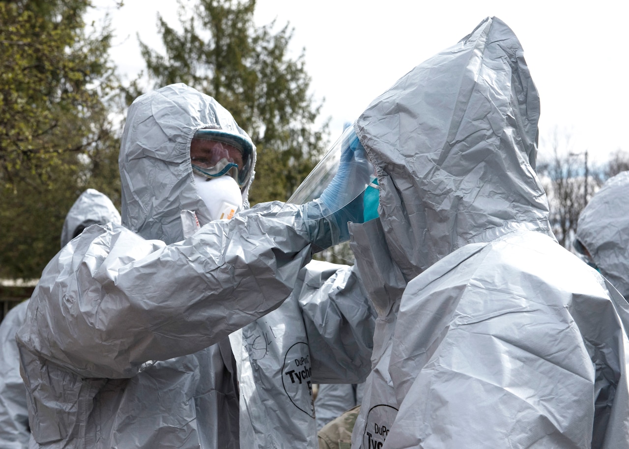 A service member checks another service member’s protective hood.