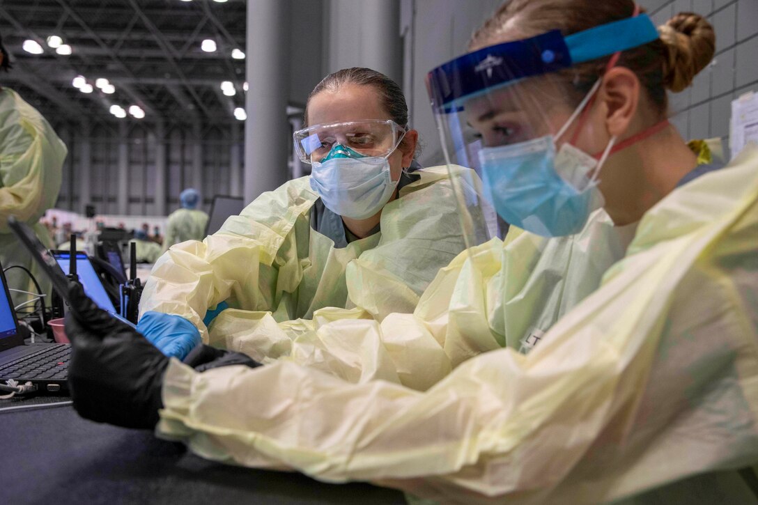 Two soldiers wearing protective gear look at tablets.