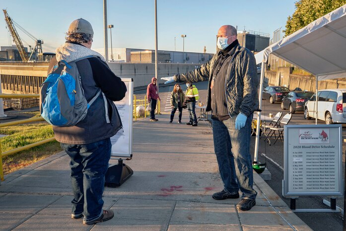 Brian Grover, right, an instructor with Code 900T, screens employees Monday, April 13 as they enter the State Street Gate to make sure they’ve completed their daily COVID-19 self-assessment before starting work at Puget Sound Naval Shipyard & Intermediate Maintenance Facility in Bremerton. (PSNS & IMF photo by Scott Hansen)