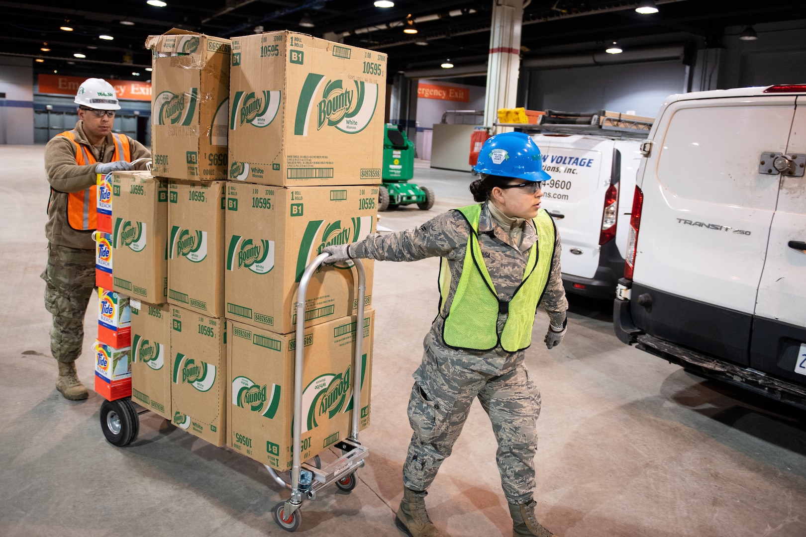 Two service members move a dolly loaded with boxes.