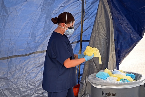 A female in hospital scrubs puts fabric into a large trash can.