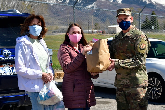 Joy Gingrich and Sarah Web, community volunteers, present Chief Master Sgt. Christopher Walker, 75th Air Base Wing Command Chief, with thousands of homemade face masks for the base military and civilian Airman personnel.