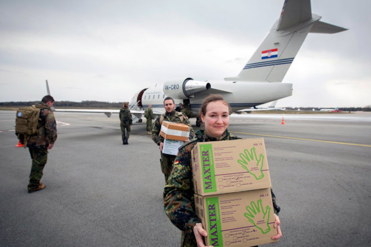 Service members carry boxes from an aircraft.