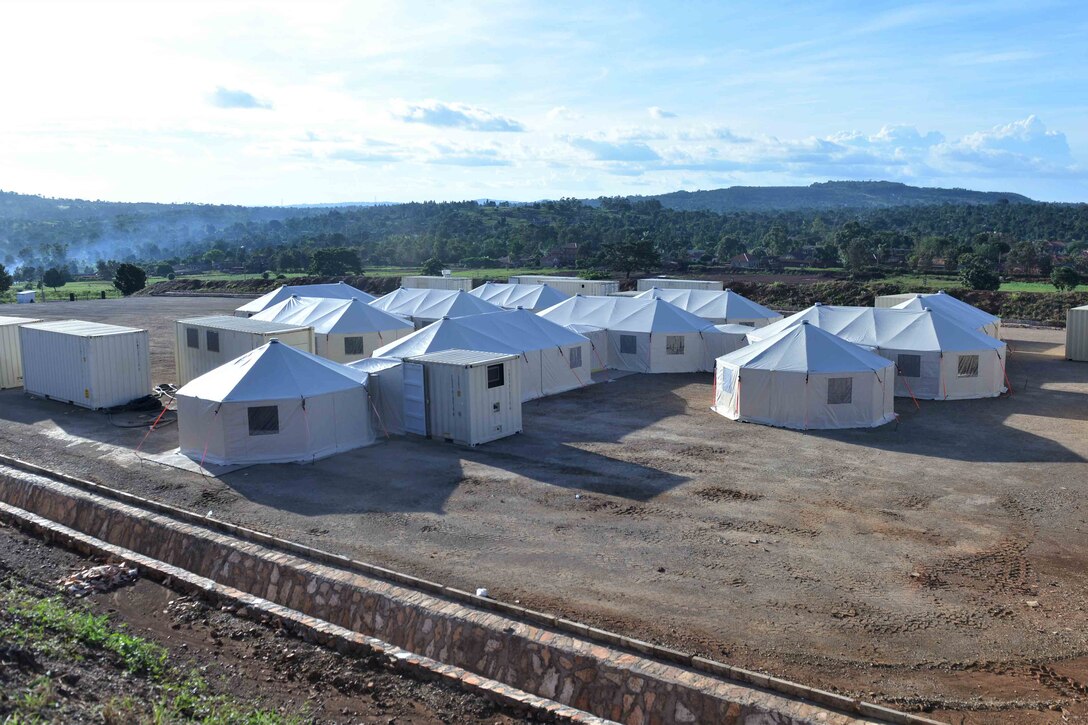 Several white tents and portable buildings in a large dirt field.