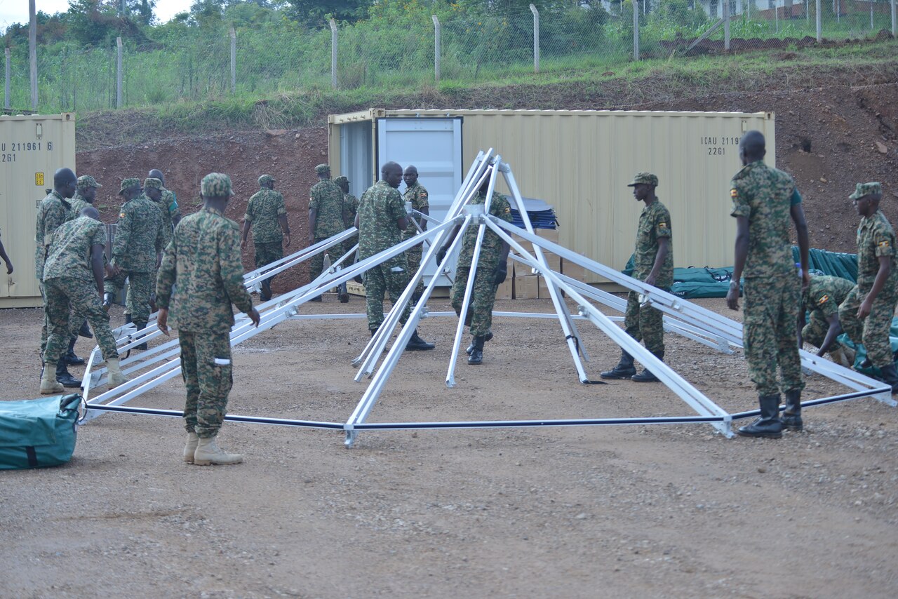 Ugandan soldiers surround a circular tent frame as they prepare to stand it up.
