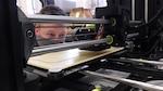 Zach Heinkel, an engineer in the Additive Manufacturing Project Office, watches an extrusion bead of a 3D printer as it makes a face mask frame on April 10, 2020, in the Additive Manufacturing Lab at Naval Surface Warfare Center Carderock Division in West Bethesda, Md.