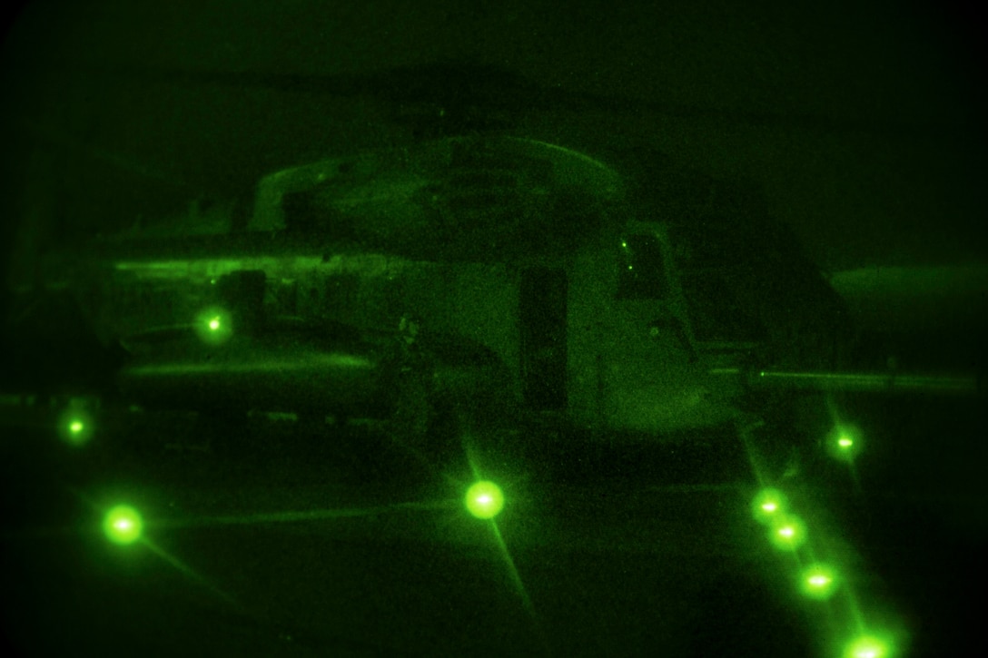 A Marine Corps helicopter, illuminated by green light, prepares for takeoff at night.