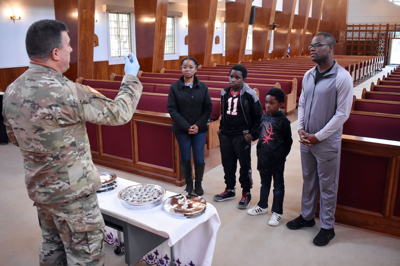 An Army chaplain holds up communion to a family of four at the front of an empty church.