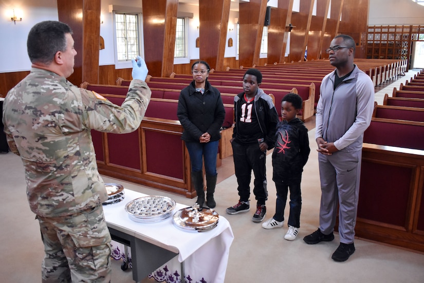 An Army chaplain holds up communion to a family of four at the front of an empty church.